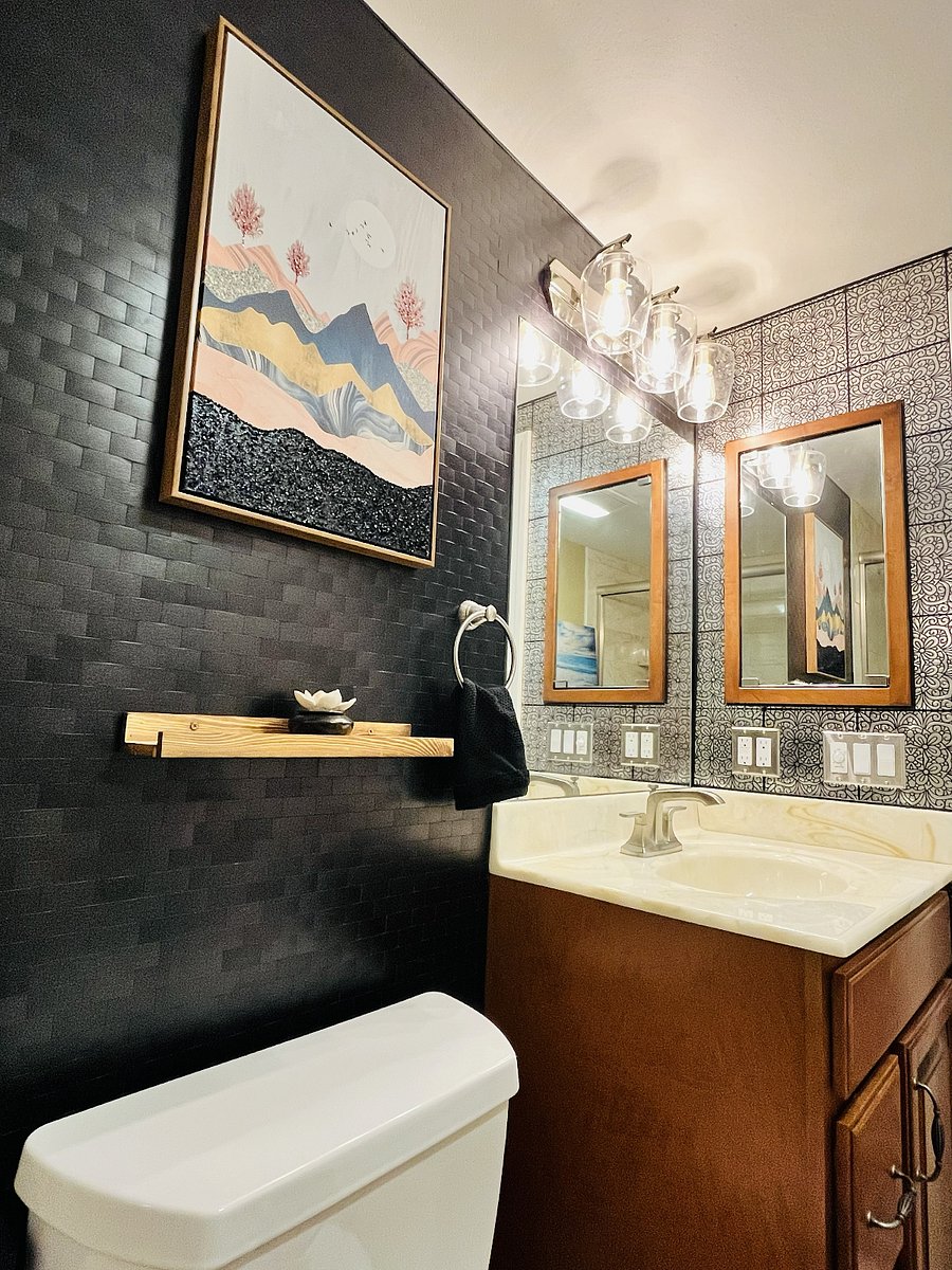 Stylish primary en suite full bathroom with a bathtub, warm wood vanity, modern lighting, generous mirror space, and refined decorative finishes.