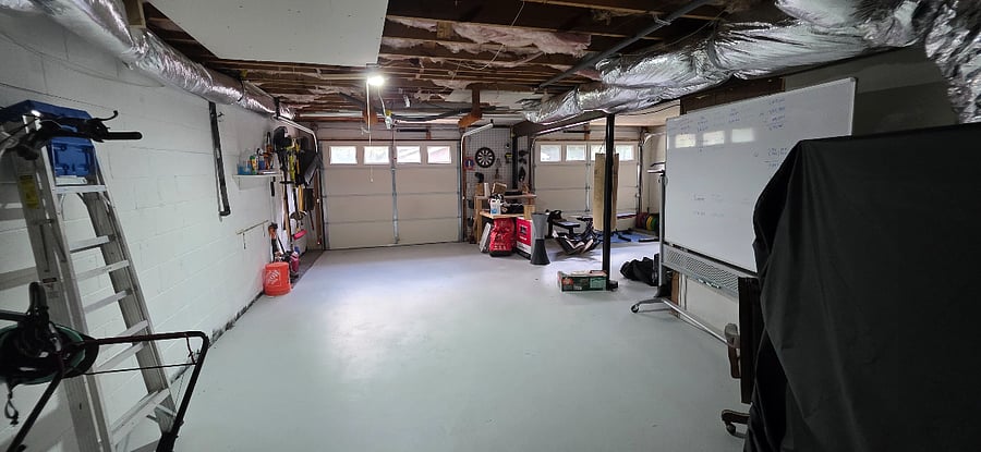 Garage with white board, gym equipment, two work benches with tools as needed. 