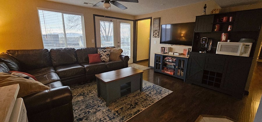 Front room with view towards smart TV, coffee/drink cabinet, microwave, ceiling fan, and entryway.