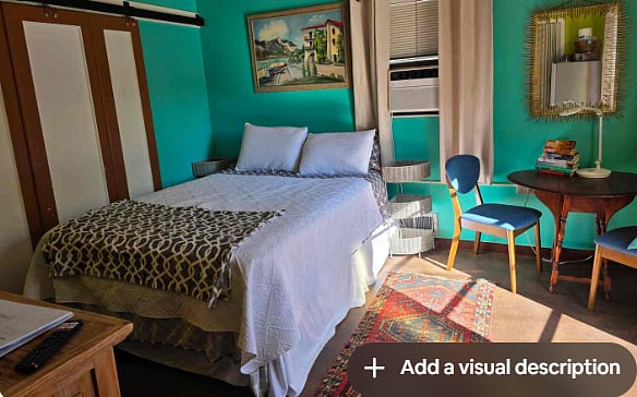 Studio with bright colors and queen bed with small dining table and two chairs.