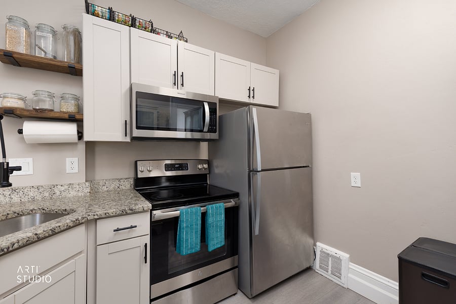 The microwave, stove, and refrigerator, with floating wooden shelves beside closed cabinet storage for a mix of open display and tucked-away space.