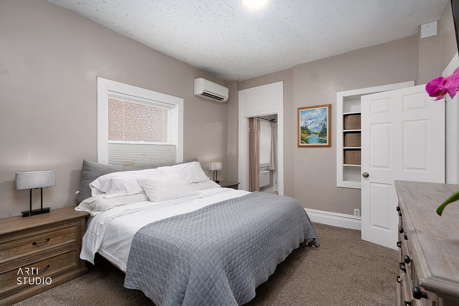The king bed anchors the primary bedroom, with built-in shelving for storage and a doorway through to the home office and a private rear entrance.