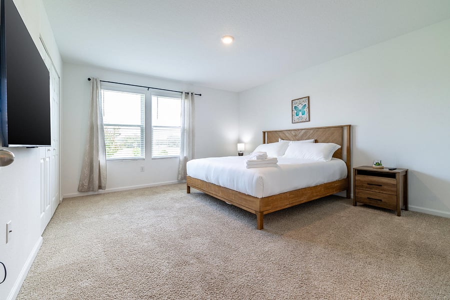 Spacious master bedroom with large windows and smart TV
