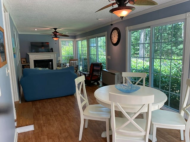 Large sunroom for living room with fireplace, tv, lounge chairs, tables, and sofa. Other side of room as additional table with seating.