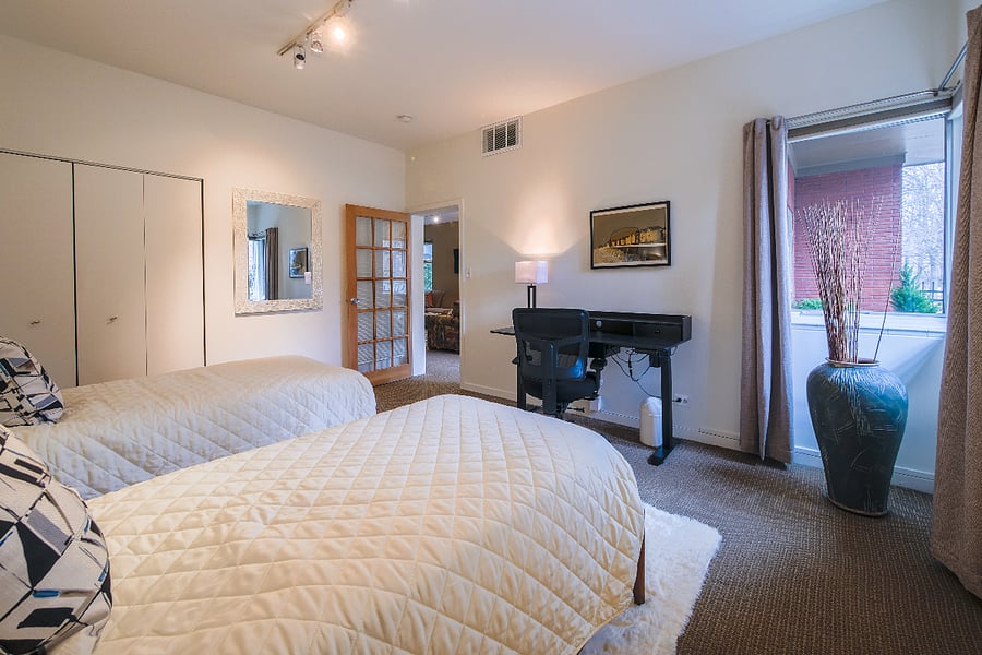 Large bedroom, with twin beds and closet and desk/TV looking onto patio and park
