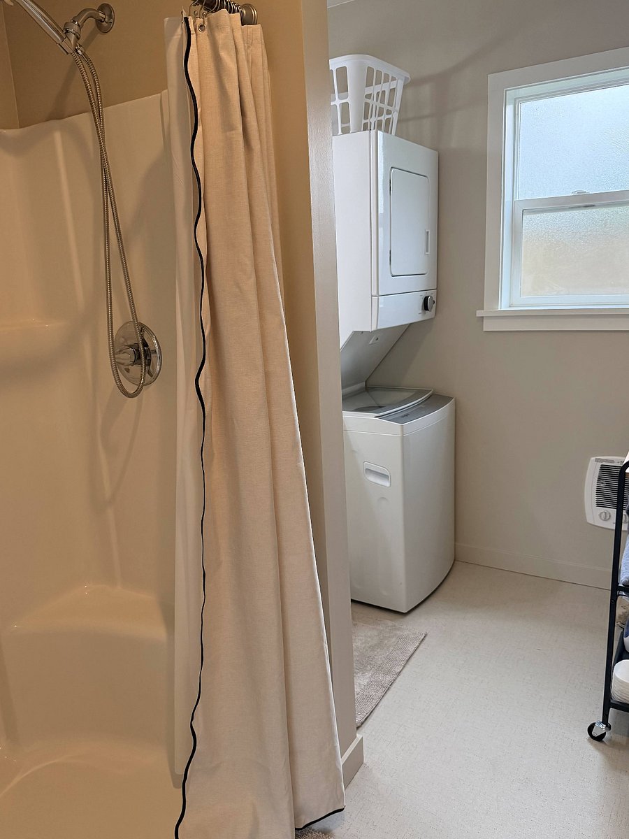 Spacious bathroom with shower, new washer/dryer, storage cart, and ample vanity storage.