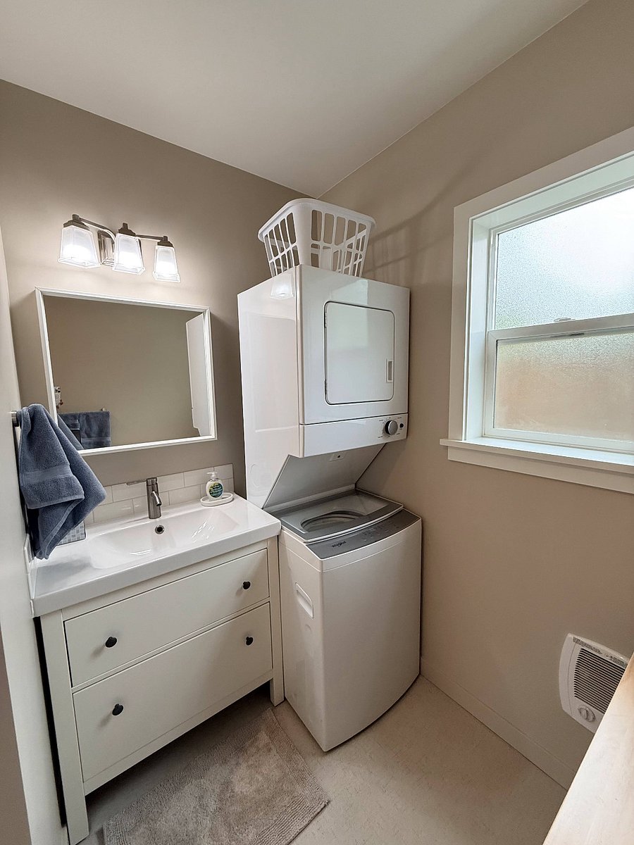 Spacious bathroom with shower, new washer/dryer, storage cart, and ample vanity storage.
