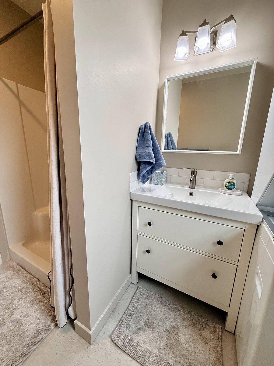 Spacious bathroom with shower, new washer/dryer, storage cart, and ample vanity storage.
