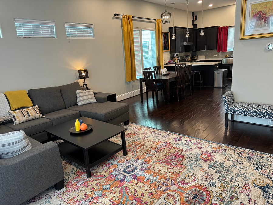 Open floor plan living room sectional sofa with behind sofa tables, side table, and lamp adjacent to dining room with 6-seat table and 3-barstool bar top