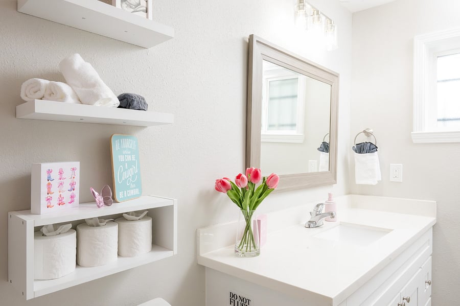 Complete bathroom with a clean white vanity, charming floating shelves for organized essentials, and thoughtful floral accents.