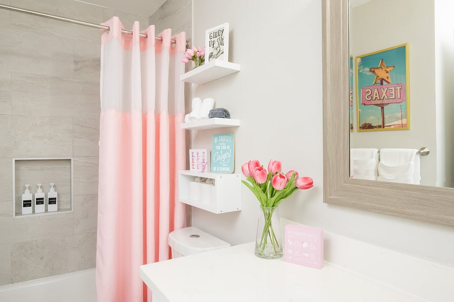 This beautiful bathroom offers a cheerful and clean environment, featuring handy built-in shower shelving and a soft pink aesthetic.