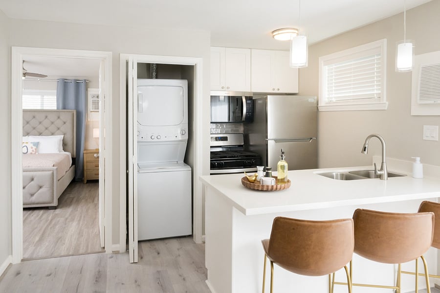 A modern and compact living space featuring a chic kitchen island with brown leather barstools and a stacked washer-dryer.