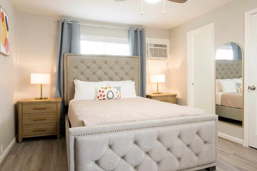 This chic and inviting bedroom features a luxurious grey tufted bed and matching chest, illuminated by twin gold lamps.
