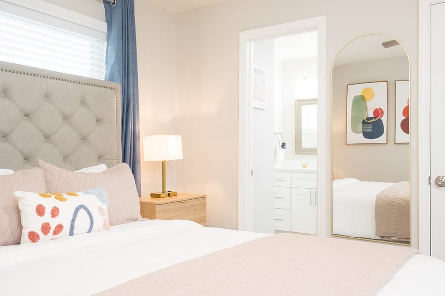 Serene bedroom with a trendy arch floor mirror and convenient en-suite bathroom access.