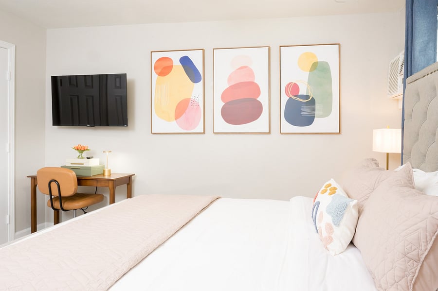 Bright master bedroom featuring a playful triptych of abstract geometric art and a working desk.