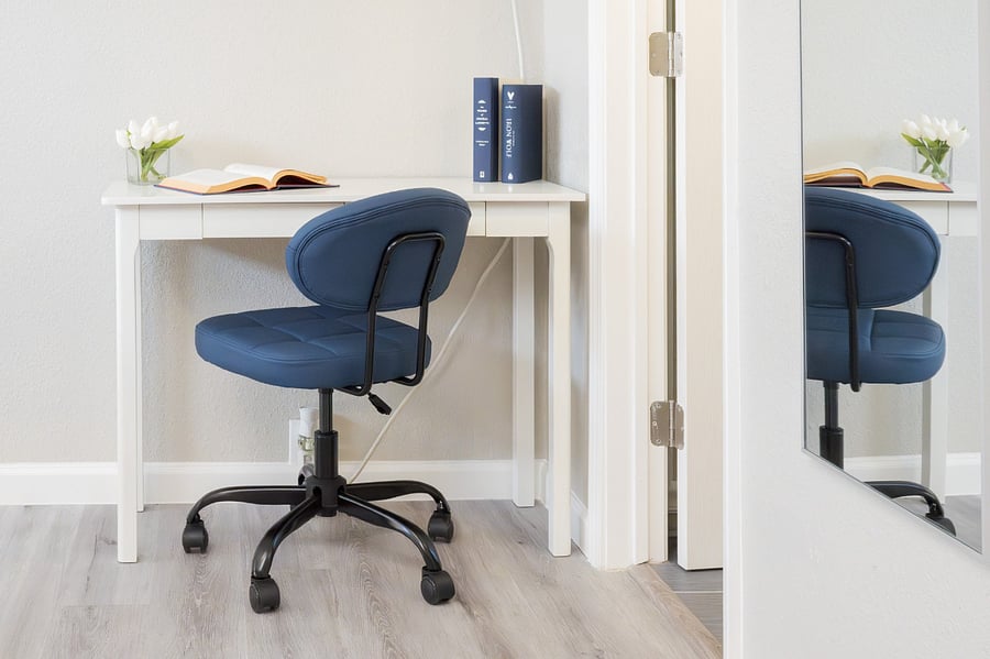 Quiet workspace featuring a clean white desk, a supportive navy blue chair, and a bright ambiance for productive thinking.