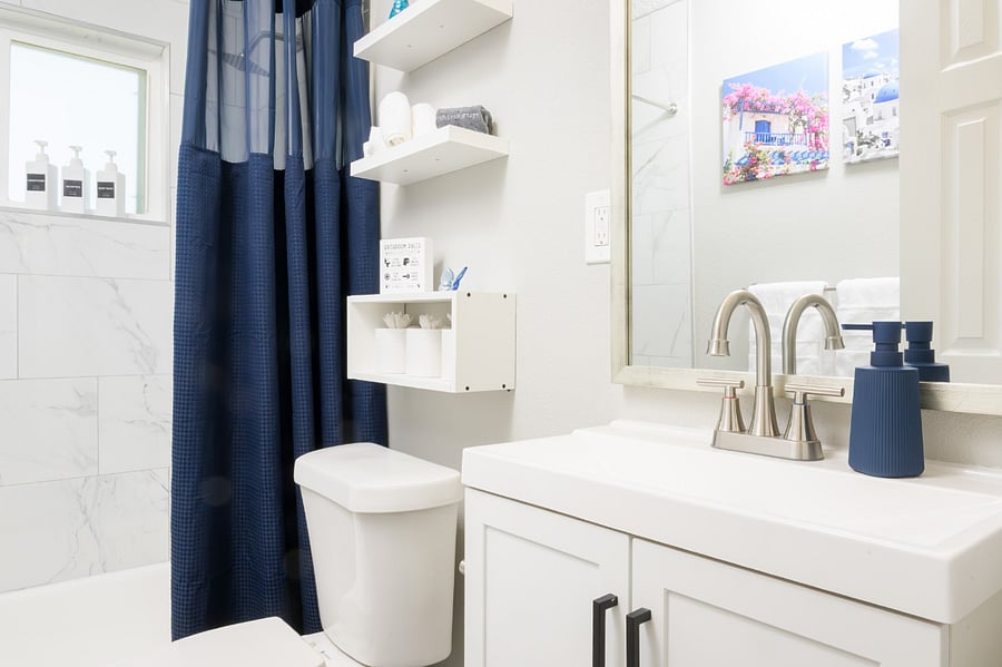 Clean bathroom with crisp white cabinetry, minimalist floating shelves and a deep navy shower curtain.