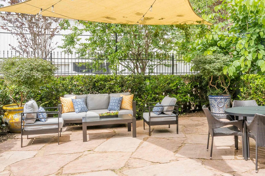 Unwind in this spacious stone patio oasis, featuring comfortable lounge seating with vibrant cushions, a dedicated outdoor dining area, and charming string lights for a perfect evening ambiance.