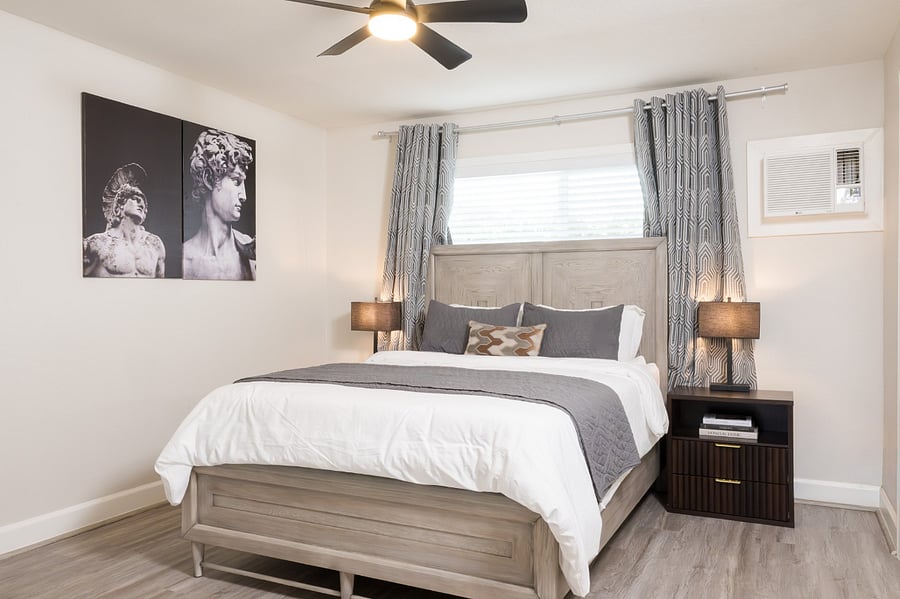 Stylish bedroom with a large bed with a light wood frame, premium linens, and striking classical bust artwork.