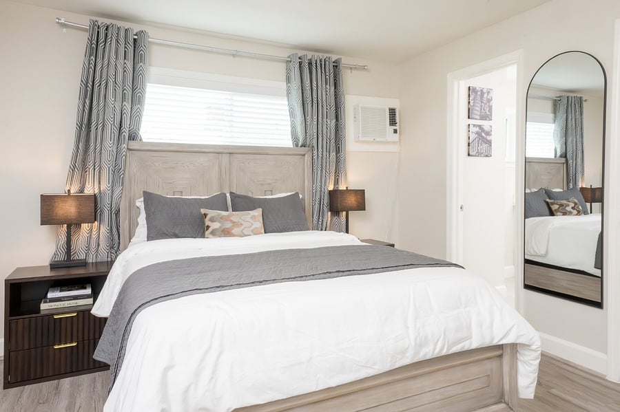 Bedroom with a plush king-sized bed with crisp white linens, modern dark wood nightstands and an arched full-length mirror.