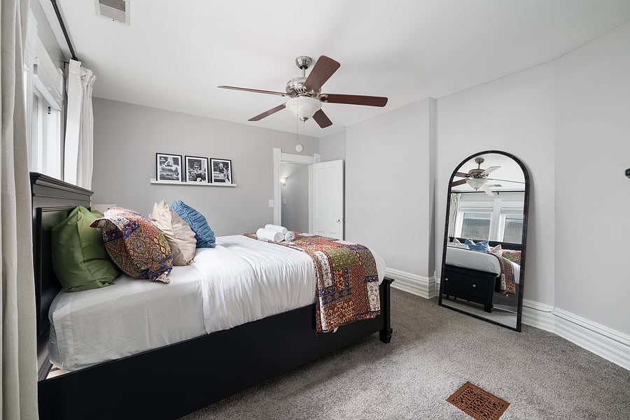 Spacious queen bedroom with fresh linens and a full-length mirror