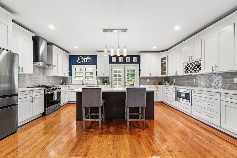 The spacious kitchen features quartz countertops, an expansive dark espresso center island, white shaker cabinetry, a timeless tile backsplash, a new refrigerator (2026), a new slide-in gas range (2026), and an upgraded dishwasher (2024).