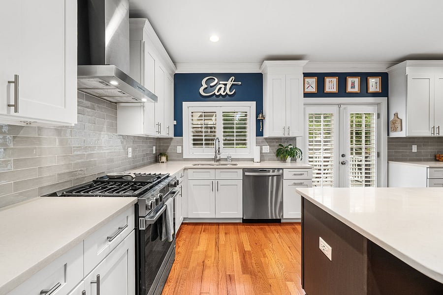 The spacious kitchen features quartz countertops, an expansive dark espresso center island, white shaker cabinetry, a timeless tile backsplash, a new refrigerator (2026), a new slide-in gas range (2026), and an upgraded dishwasher (2024).