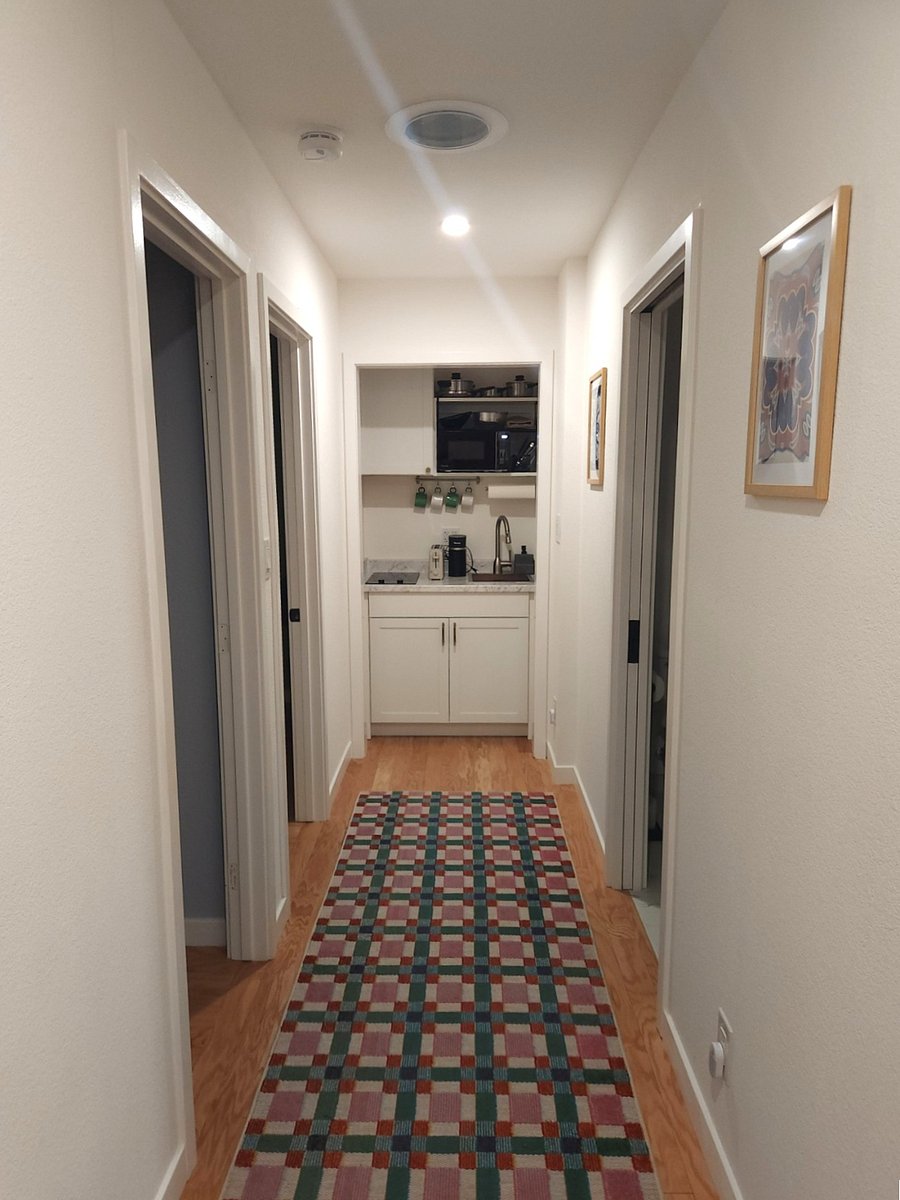 Kitchenette at the end of the hallway, which is hardwood floors. Entrances to living room and bedroom on the left. Bathroom entrance to the right.