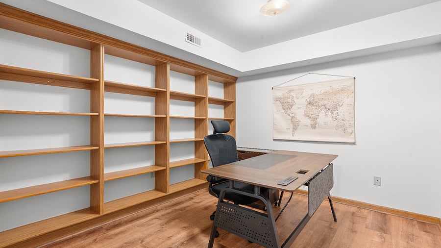 Dedicated basement office with a spacious desk, ergonomic chair, and extensive built-in shelving for a comfortable and organized workspace.