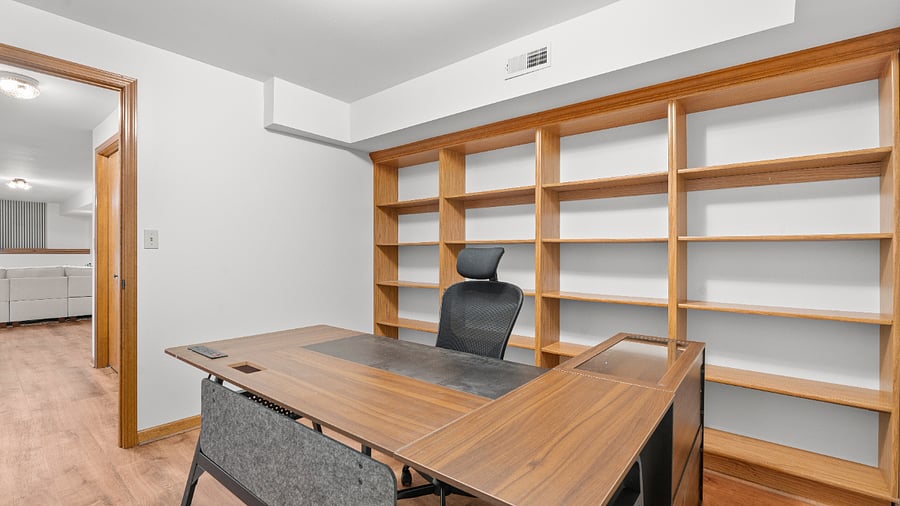 Dedicated basement office with a spacious desk, ergonomic chair, and extensive built-in shelving for a comfortable and organized workspace.