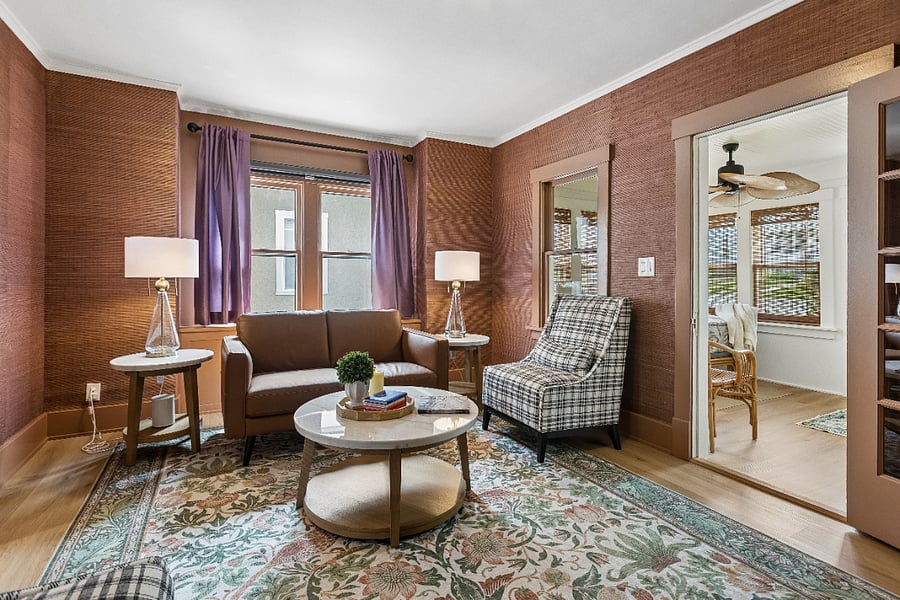 The inviting living room blends historic character with boutique comfort, featuring rich bamboo wallpaper and a premium Natuzzi Italian leather loveseat.