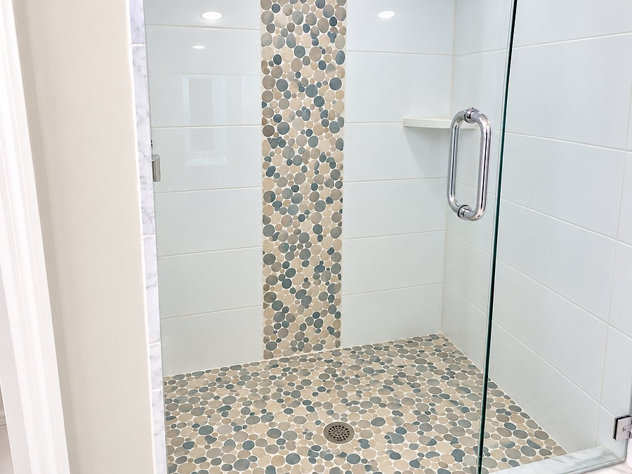 A separate glass-enclosed shower with decorative stone detail adds convenience to the primary bath.