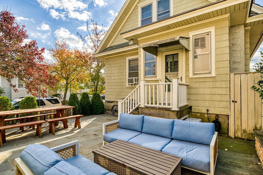 Backyard patio has outdoor seating, large picnic table, 2 large umbrellas and gas grill.