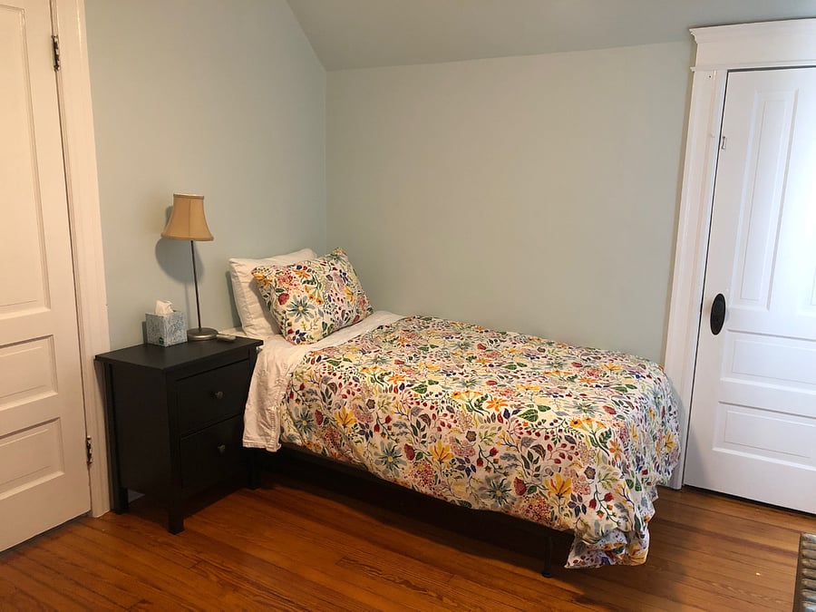 Front bedroom has twin bed, ceiling fan, bedside table, dresser, Ikea Poang easy chair, desk and desk chair.