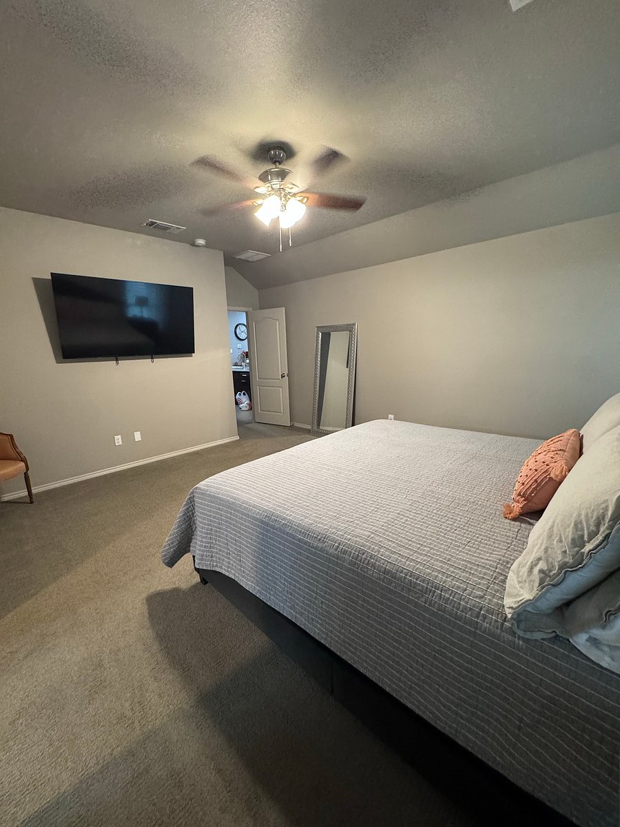 Master bedroom includes: king sized bed, nightstands, full length mirror, small chair, and mounted TV