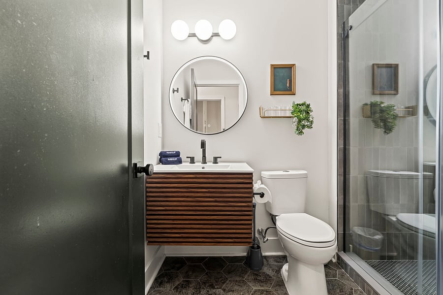 A modern bathroom with a warm wood vanity, round mirror and walk-in shower, designed to feel fresh and spa-like every morning.