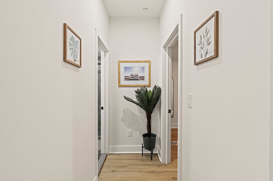 A quiet hallway with greenery and art leads to your private bedroom and bathroom, tucked away for real rest and privacy.
