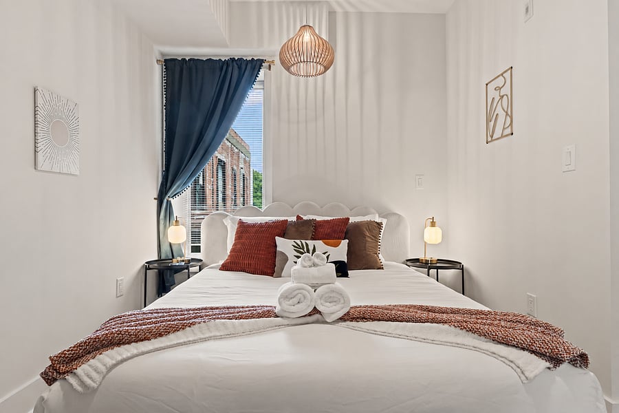Open the curtains to natural light and a warm boho bedroom with a padded headboard, matching nightstands and lamps on both sides of the queen bed.