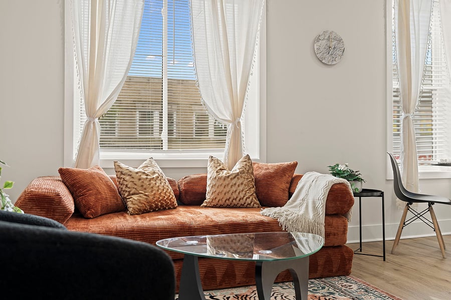 Sink into the plush rust velvet sofa with soft throws and boho pillows, the perfect spot to decompress with sheer curtains glowing in the afternoon light.
