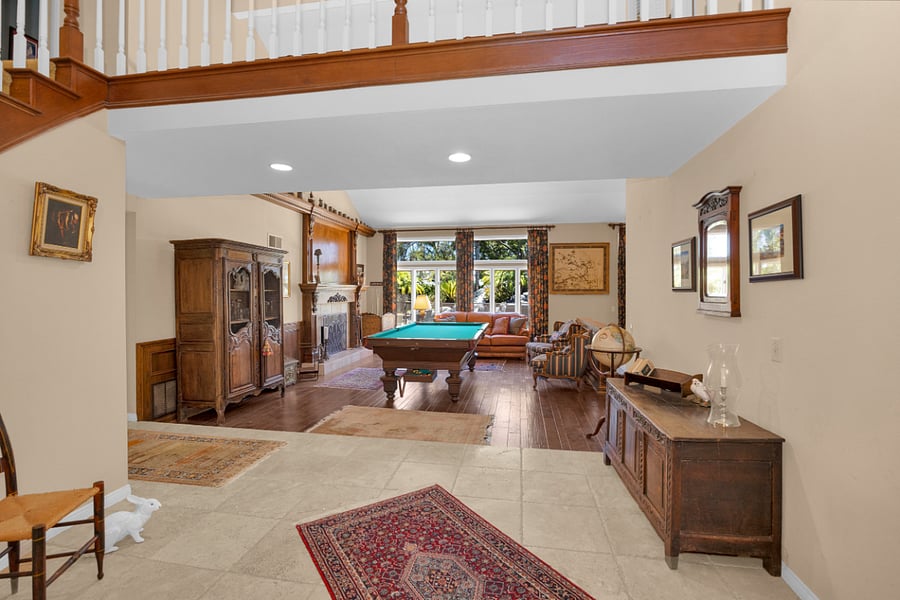 Inviting entertainment space with a pool table, comfortable seating, fireplace, and plenty of natural light overlooking the backyard.