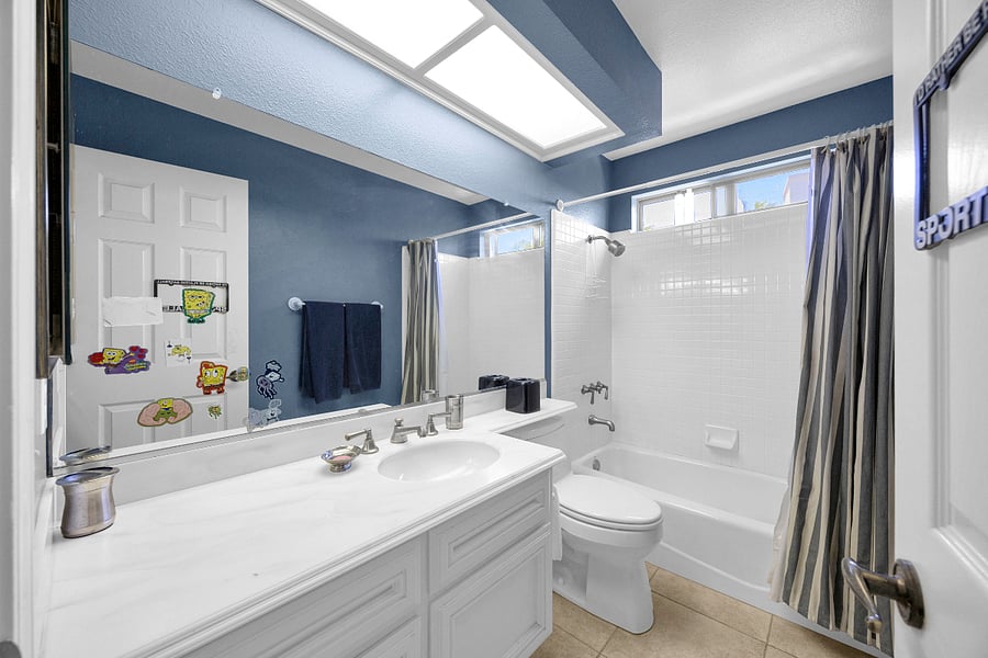 Private ensuite bathroom with a bright vanity, large mirror, skylight, and a full tub/shower combination.