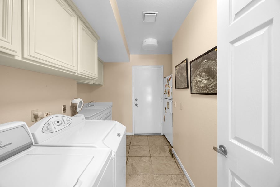 Convenient laundry room with a full-size washer and dryer, utility sink, ample storage, and direct access to the garage.