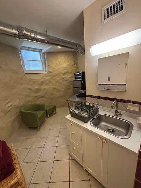 Sink doubles for the bath and kitchenette; fridge, toaster oven, induction hot plate, and comfy chair with ottoman.