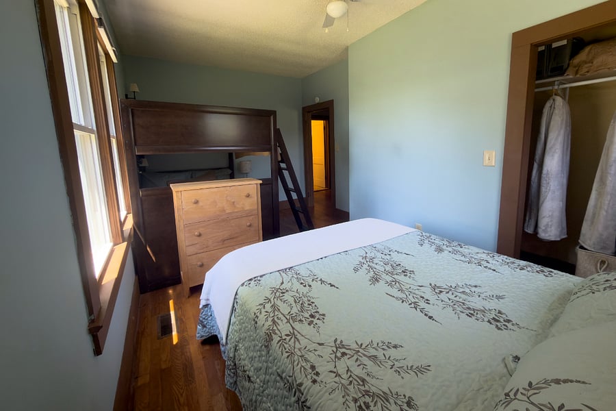 The second bedroom from the other side dresser, closet with extra linens, and morning light through original windows.