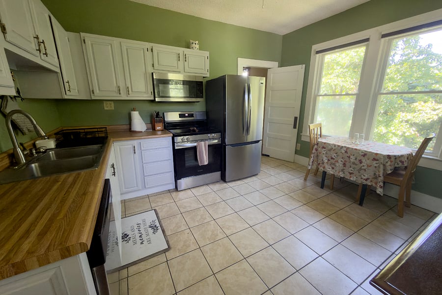 The full kitchen from the mudroom all new appliances, butcher block counters, and an original swing door that's been separating kitchens from dining rooms since the house was built.