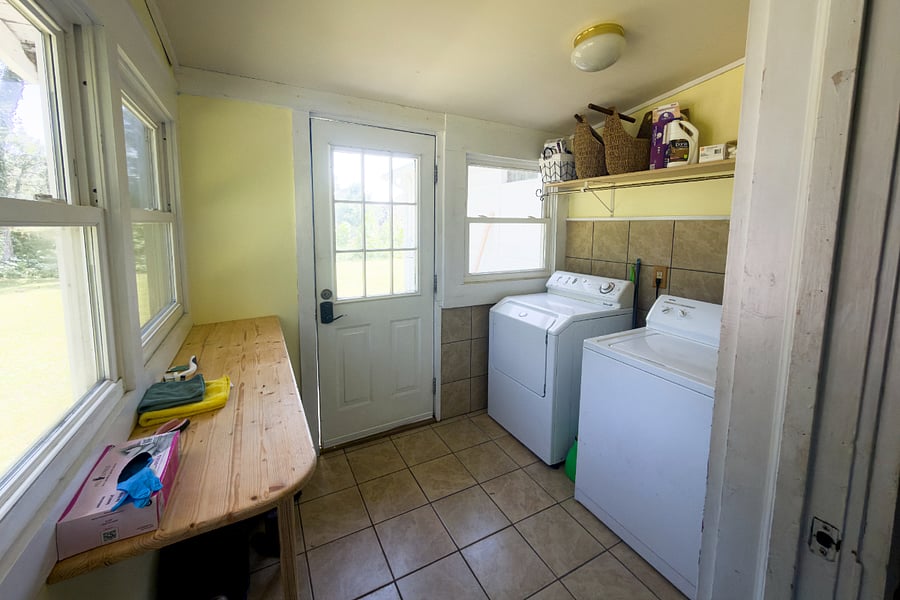 The mudroom pulls double duty washer and dryer, a built-in workbench for gear and projects, windows on two sides, and a back door that leads directly to the yard and lockable storage.