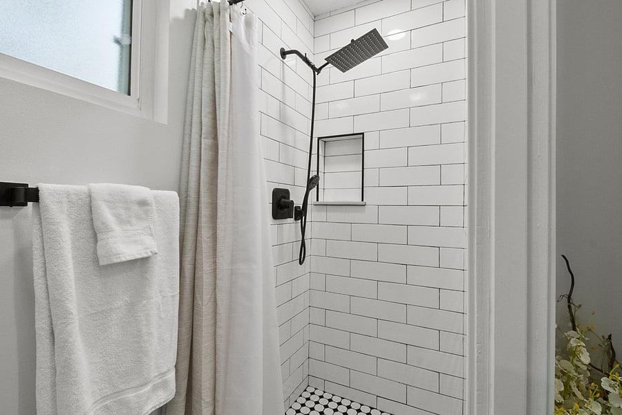 Clean tiled shower with rainfall showerhead and handheld sprayer.