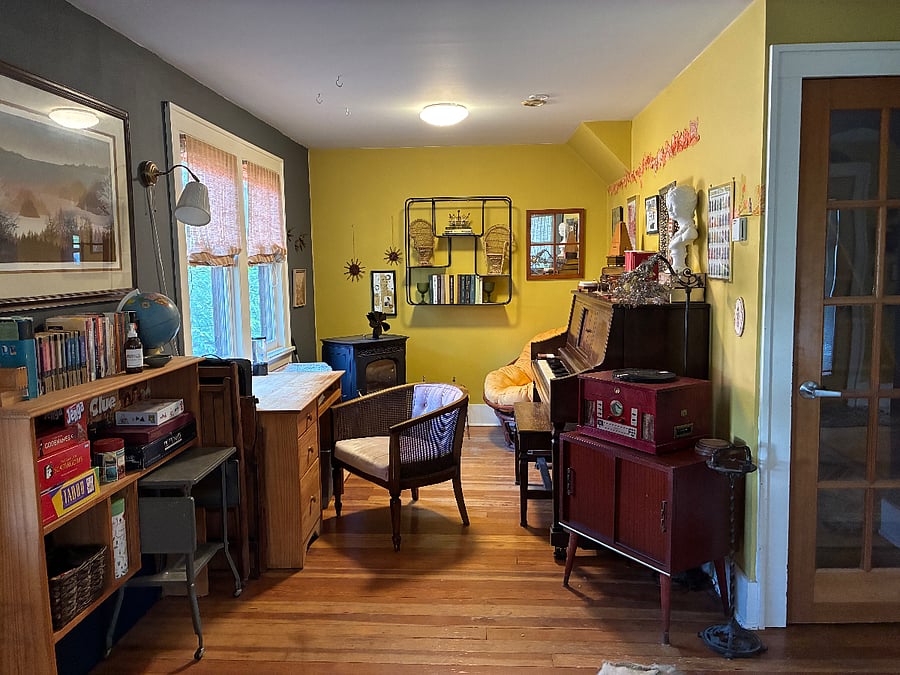 Around the corner from the living room is a cozy living space: a desk by the window, a papasan chair by the pellet stove, and plenty of games to play and books to read. Door on the right leads upstairs.