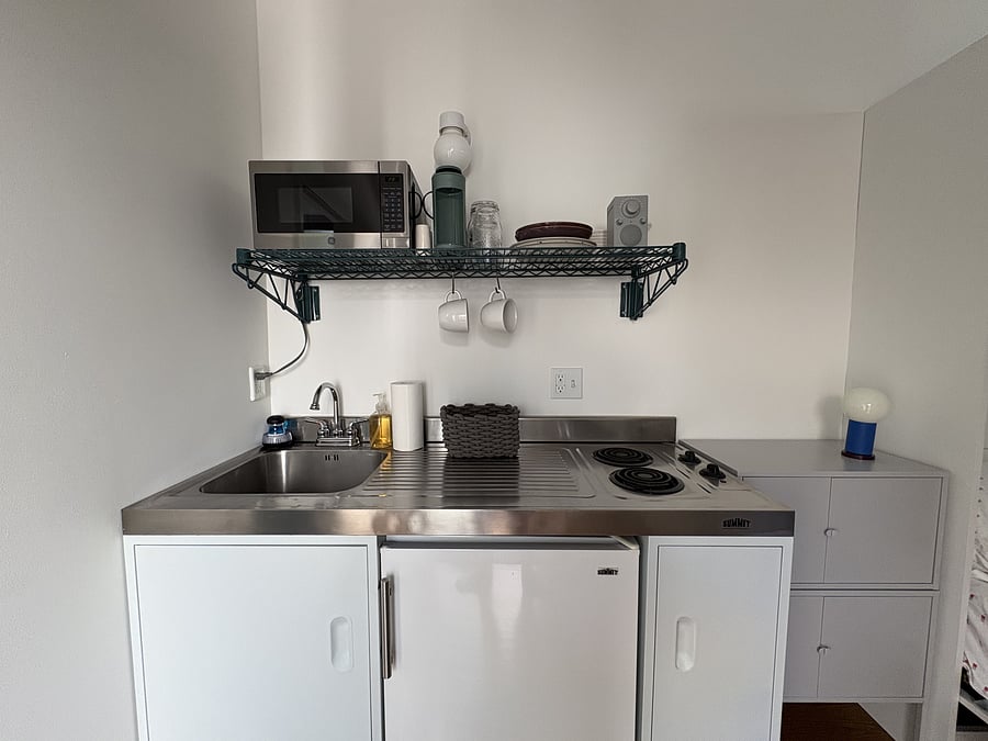 Kitchenette with sink, dual electric burners, microwave, mini fridge, coffee maker, basic dish ware, glassware, and kitchen prep items. To the right, clothing cabinet.