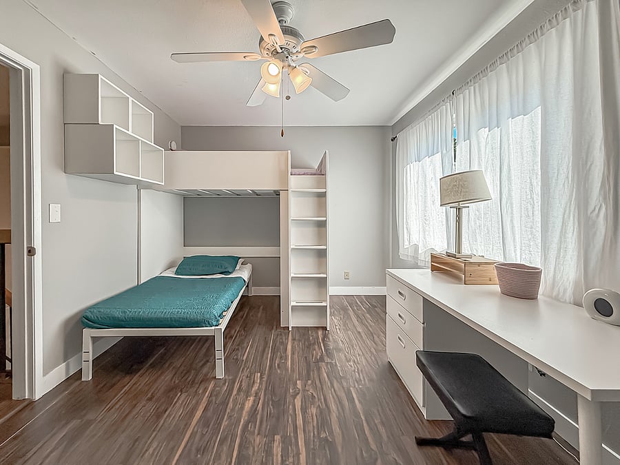 Spacious furnished bedroom with wood flooring, floor-to-ceiling window, private balcony, updated decor, and ample space for sitting area and storage.